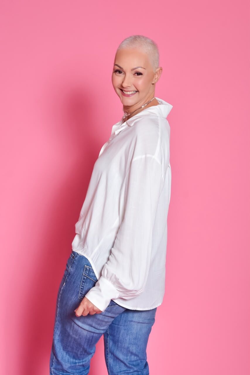 Mulher sorrindo com a cabeça raspada e camisa branca