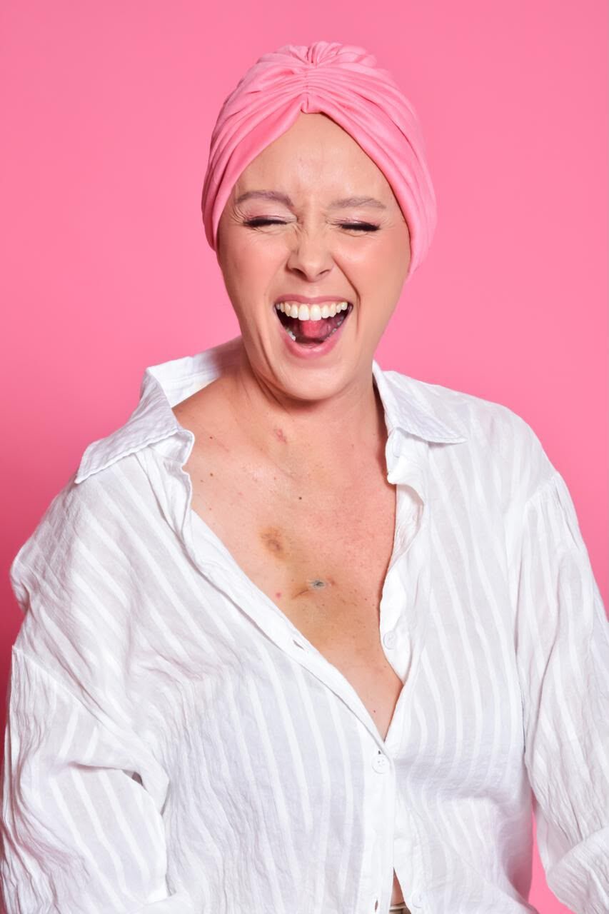 Mulher sorrindo de olhos fechados, com lenço rosa na cabeça